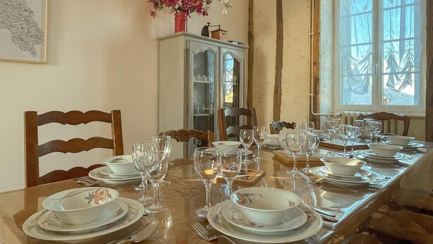 A dining room with a wooden table set for a meal, a cabinet with a vase of flowers, and a window with curtains.