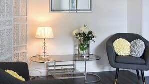 A modern living room with a glass coffee table, a grey armchair, a white lamp, and a vase with white flowers. - The Coach House at Mount Pleasant (Heighington, near Darlington)