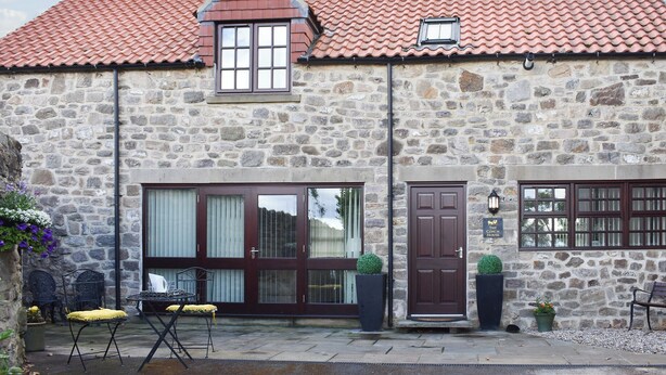 A stone building with a red-tiled roof, a large window, and a door. There are outdoor seating areas with chairs and tables. - The Coach House at Mount Pleasant (Heighington, near Darlington)