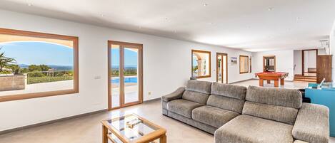 A spacious living room with a large sofa, a glass coffee table, and a view through the sliding glass doors.