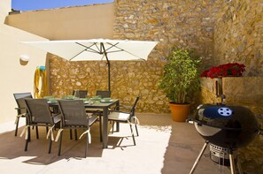 Eine Terrasse im Freien mit einer Steinwand, einem Tisch mit Stühlen, einem Grill und einem Blumentopf.