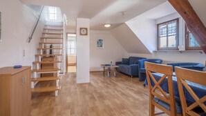Een loft-achtige kamer met een houten trap, een blauwe zithoek en een eettafel.