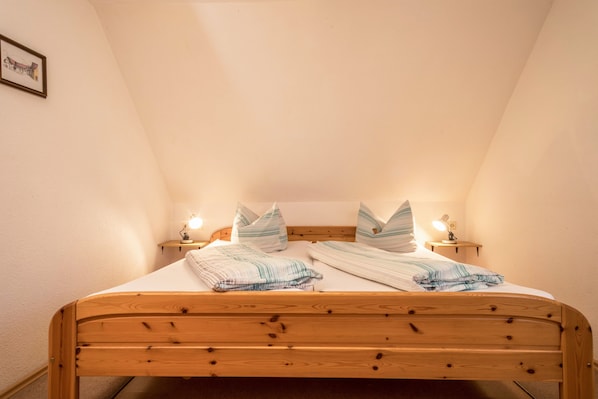 Un lit simple avec un cadre en bois, deux tables de chevet avec des lampes et un tableau encadré au mur.