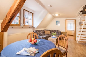 Un coin repas avec une table ronde, des chaises, un saladier de fruits et une fenêtre avec des rideaux.