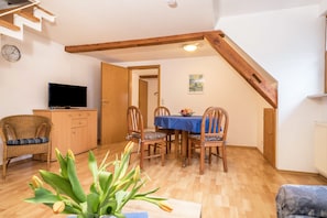 Un coin repas avec une table dressée pour quatre personnes, des chaises en bois, un téléviseur posé sur un meuble et un escalier.