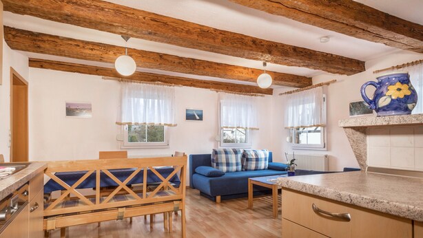 A cozy living area with a wooden bench, blue sofa, and a kitchen with a granite countertop. - Apartment “4-Star Holiday Apartment No. 3” with Wi-Fi, Balcony, Garden & Terrace (Deggenhausertal)