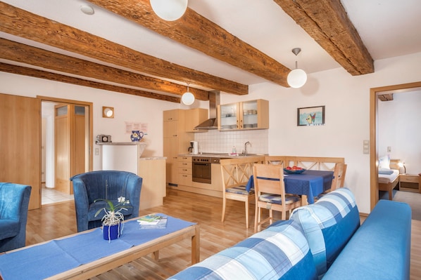 A cozy living room with a sofa, a dining table, and a kitchen area with wooden beams and cabinets.