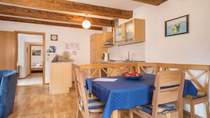 A kitchen with wooden beams, a dining table with blue tablecloth, wooden chairs, a fruit bowl, and a painting on the wall. - Apartment “4-Star Holiday Apartment No. 3” with Wi-Fi, Balcony, Garden & Terrace (Deggenhausertal)
