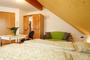 A bedroom with a bed, a green sofa, a wooden wardrobe, a small table with a vase, and a mirror.
