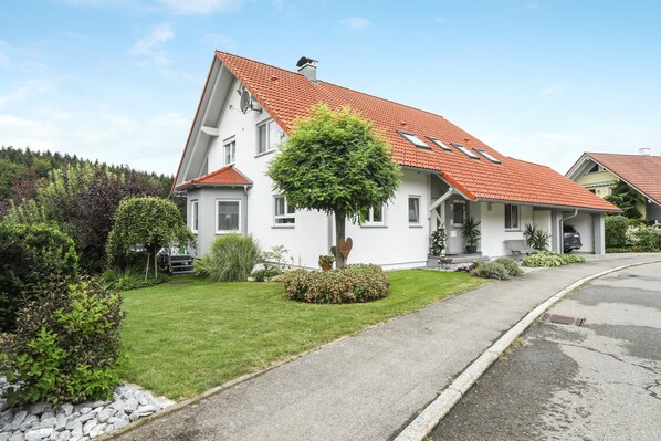 A white house with a red roof, a well-maintained lawn, and a driveway.