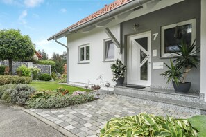 A building with a white exterior, a tiled roof, and a number '7' on the door. There are potted plants and a well-maintained garden in front.