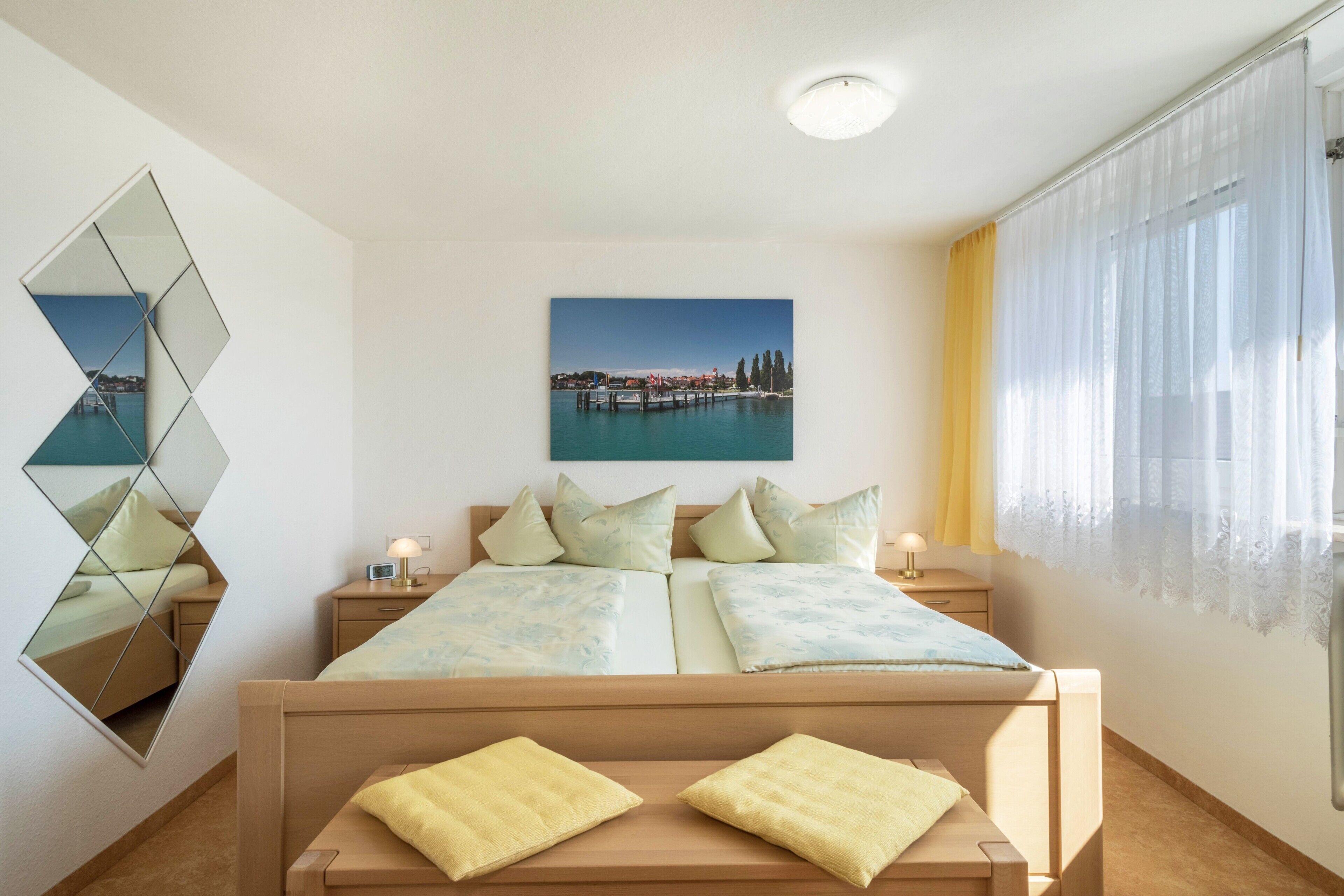 A bedroom with a bed, bedside tables, a mirror, a painting, and a window with curtains.