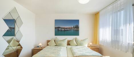 A bedroom with a bed, bedside tables, a mirror, a painting, and a window with curtains.
