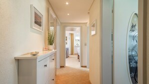 Un pasillo con un aparador blanco, un cuadro enmarco y una puerta con un panel de vidrio decorativo.