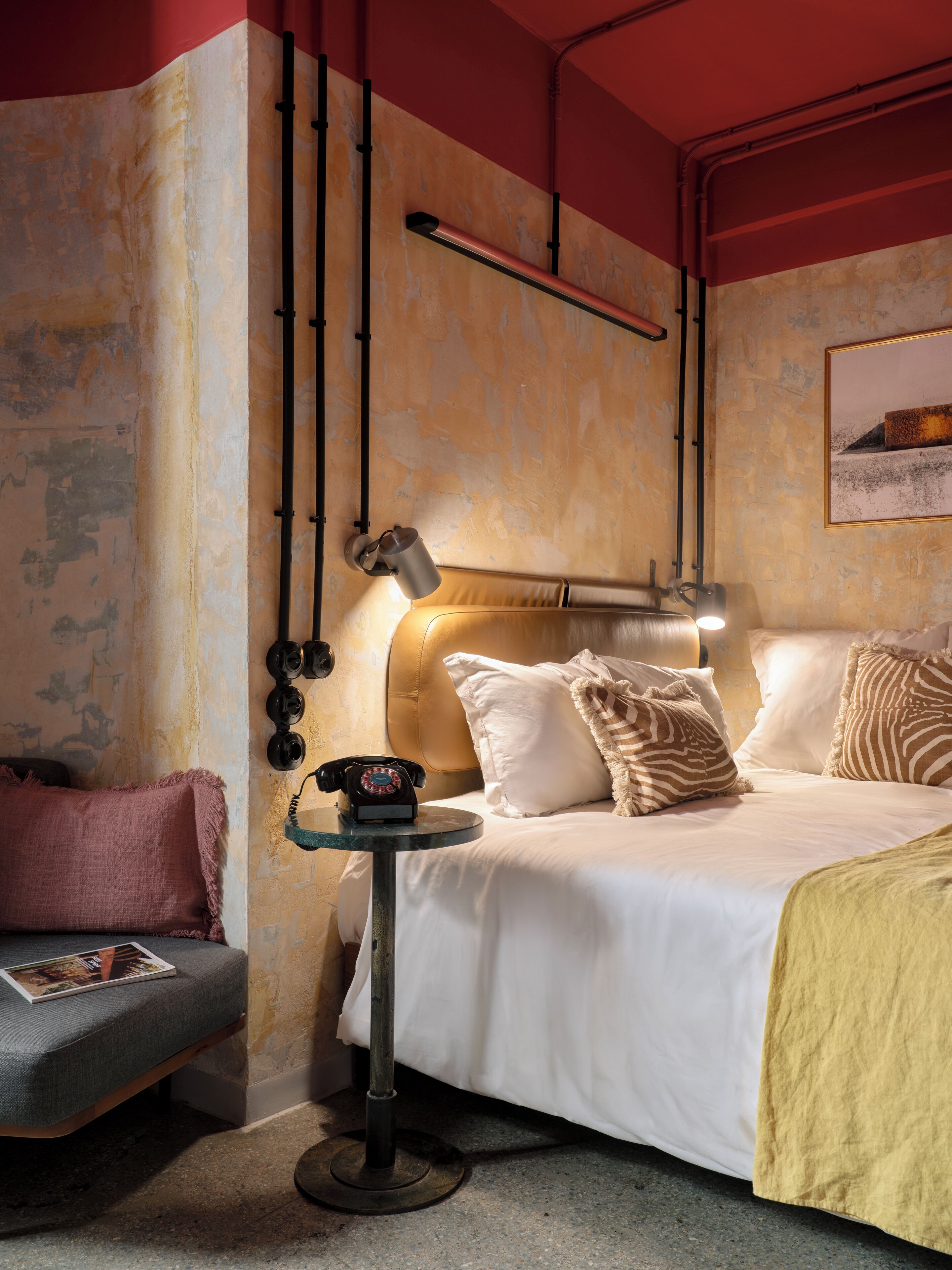 A hotel room with a bed, bedside table, lamp, telephone, and a wall-mounted light fixture.