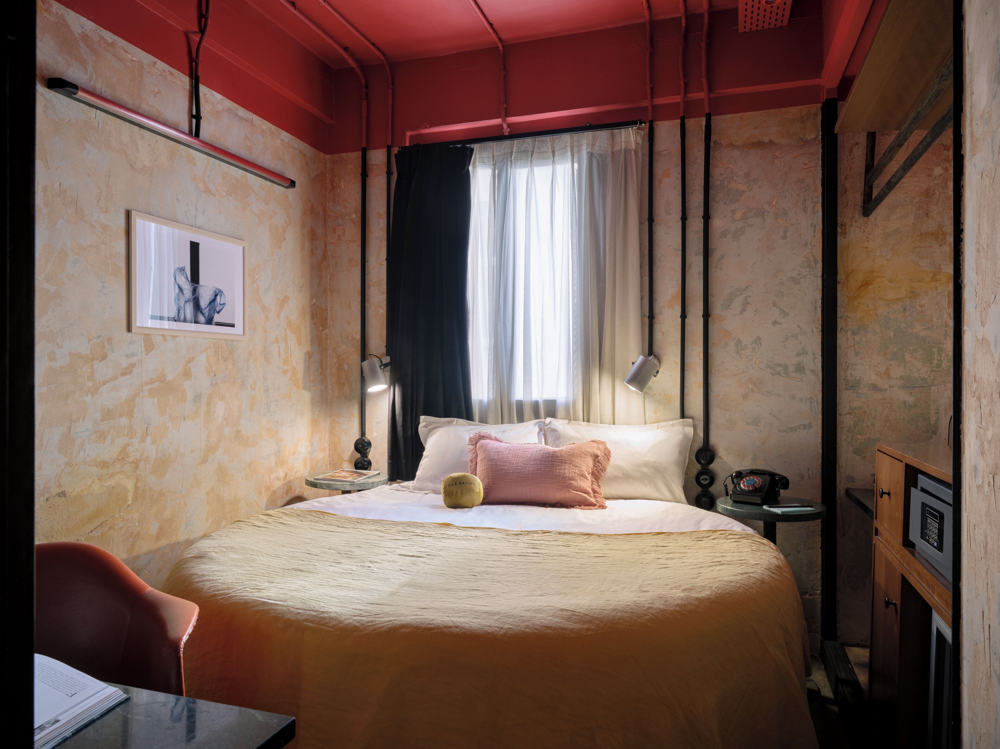 A hotel room with a bed, bedside table, lamp, and a window with curtains.