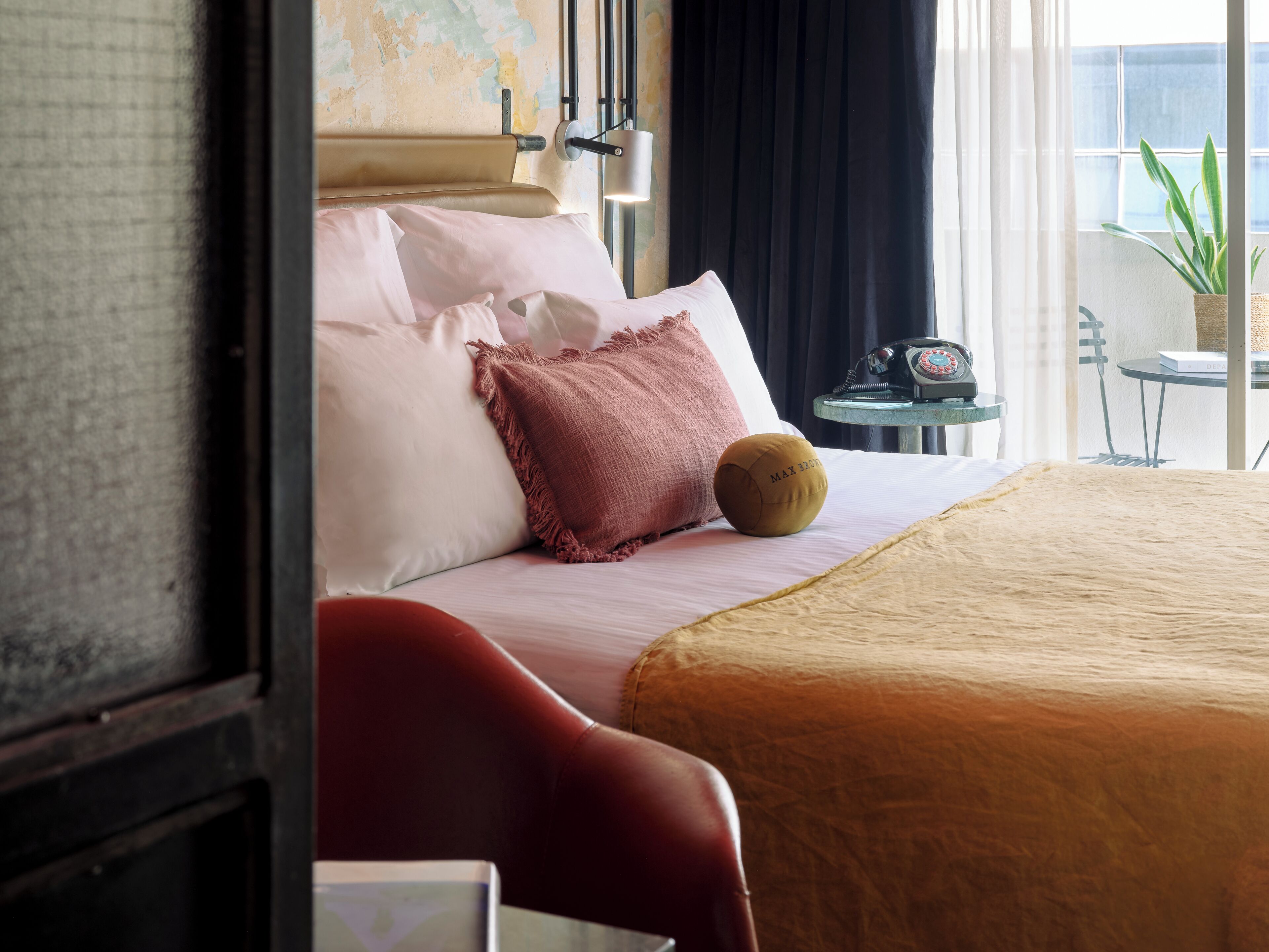 A hotel room with a bed, pillows, a small round table with a telephone, and a window with a view of the outside.
