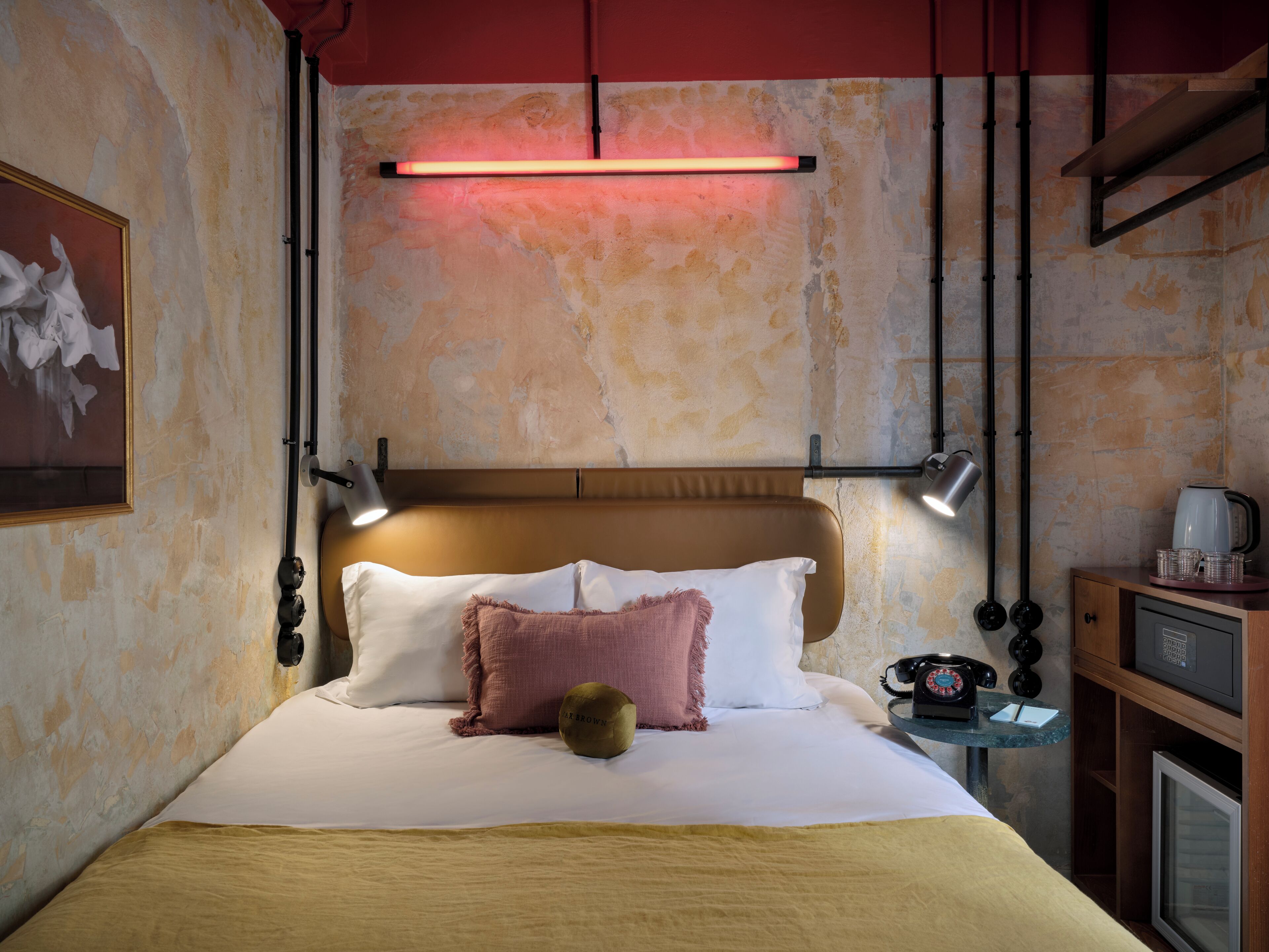 Et hotelværelse med en seng, sengeborde, lamper og en vægmonteret lampe.