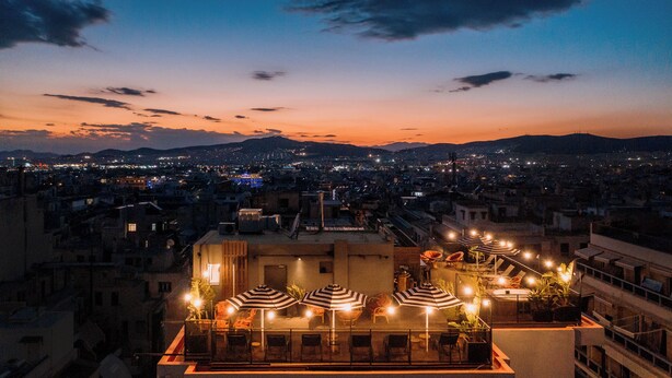 A rooftop terrace with multiple lounge chairs and umbrellas, overlooking a cityscape at dusk. -  Max Brown Hotel Downtown, part of Sircle Collection (Formally known as Dave Red) (Athens)