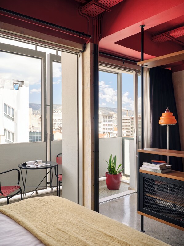 Una habitación de hotel con una cama, una mesita con una silla, una planta en maceta y una estantería.