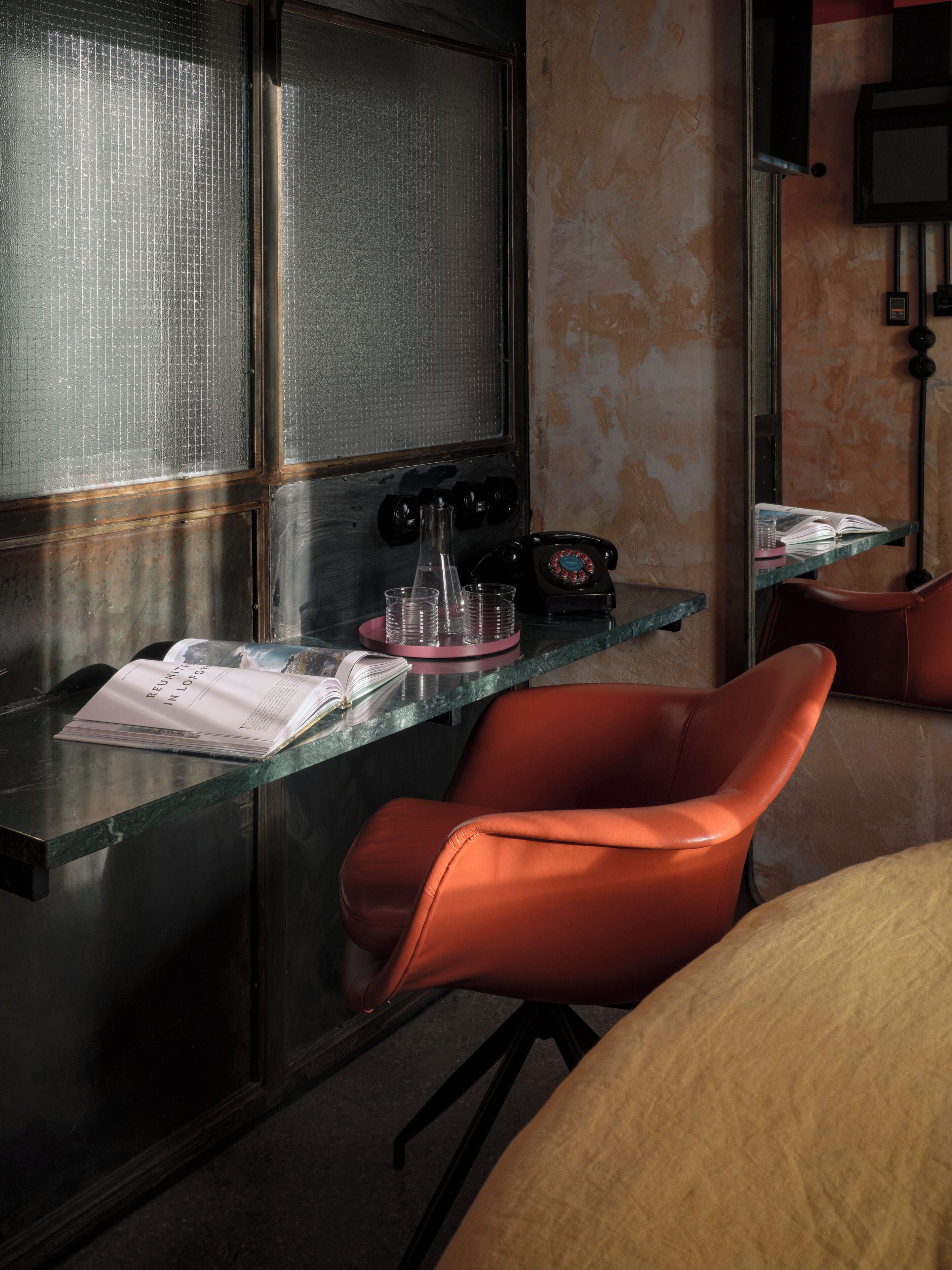 Una habitación moderna con un escritorio de cristal, una silla roja, un teléfono antiguo y un libro titulado 'Reuniting in London'.
