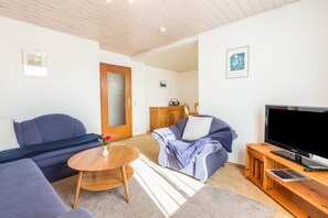 Una sala de estar con un sofá, una mesa de centro, un televisor y un mueble de madera.