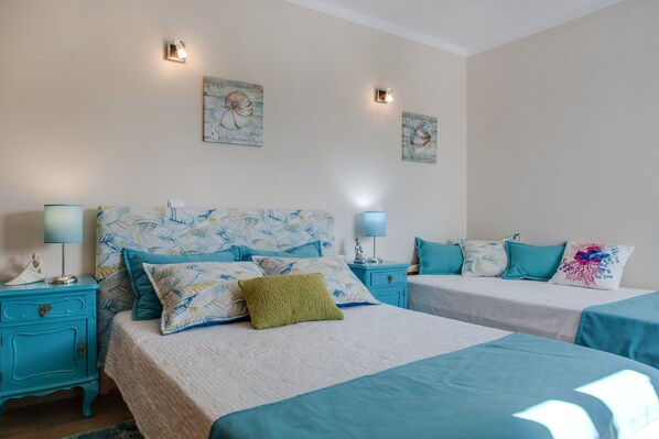 A bedroom with two beds, each with a blue bedspread and matching pillows, a nightstand with a lamp, and wall art above the beds.