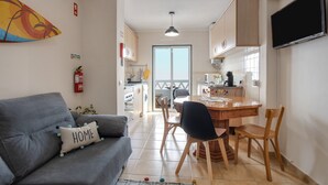 Ein Wohnzimmer mit Sofa, einem Esstisch mit Stühlen, einer Küchenzeile und einem großen Fenster.