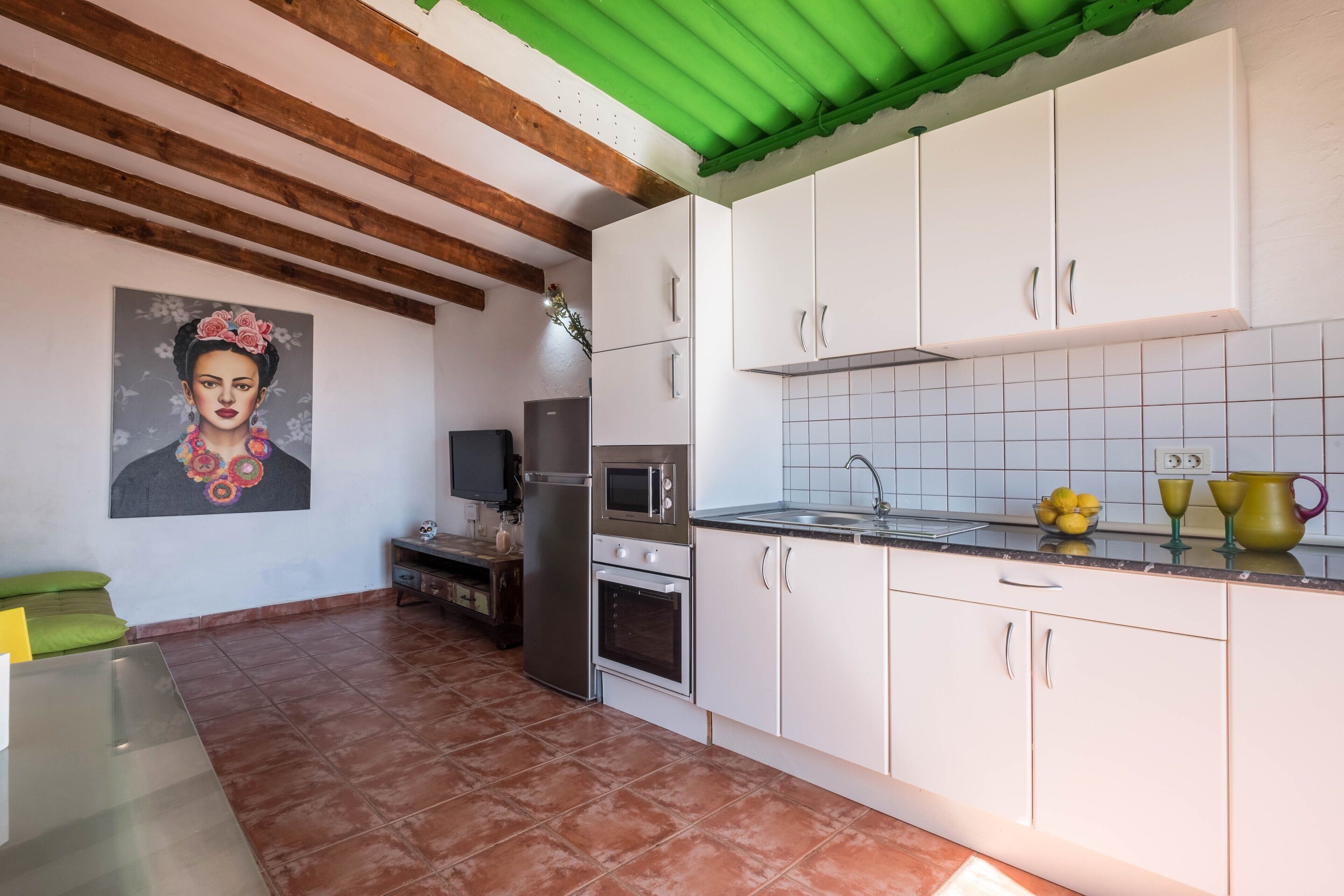 Una cocina con armarios blancos, un refrigerador de acero inoxidable, un microondas y una salpicadura trasera de azulejos.