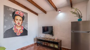 Un soggiorno con televisore, frigorifero, mobiletti in legno e un quadro appeso al muro.