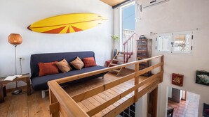 Una habitación con sofá, una tabla de surf, una escalera y una barandilla de madera.