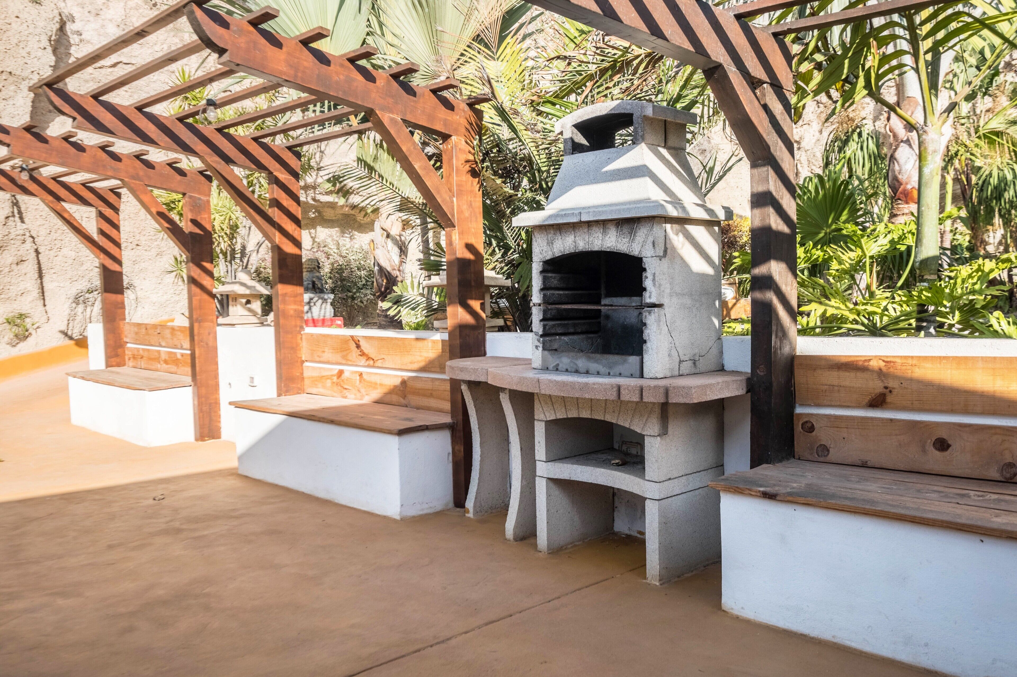 Une terrasse extérieure dotée d’un four à pizza en pierre, d’une pergola en bois et de bancs blancs.