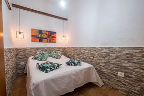 A bedroom with a bed, colorful pillows, a wall art piece, and two hanging light fixtures.