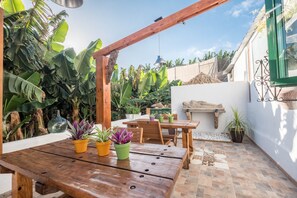 Una pérgola de madera, una mesa de madera con plantas en macetas y una zona de patio con baldosas.