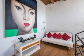 Une pièce avec un canapé blanc, des coussins rouges, un meuble blanc sur lequel est posée une planche de skate, et un grand tableau abstrait accroché au mur.
