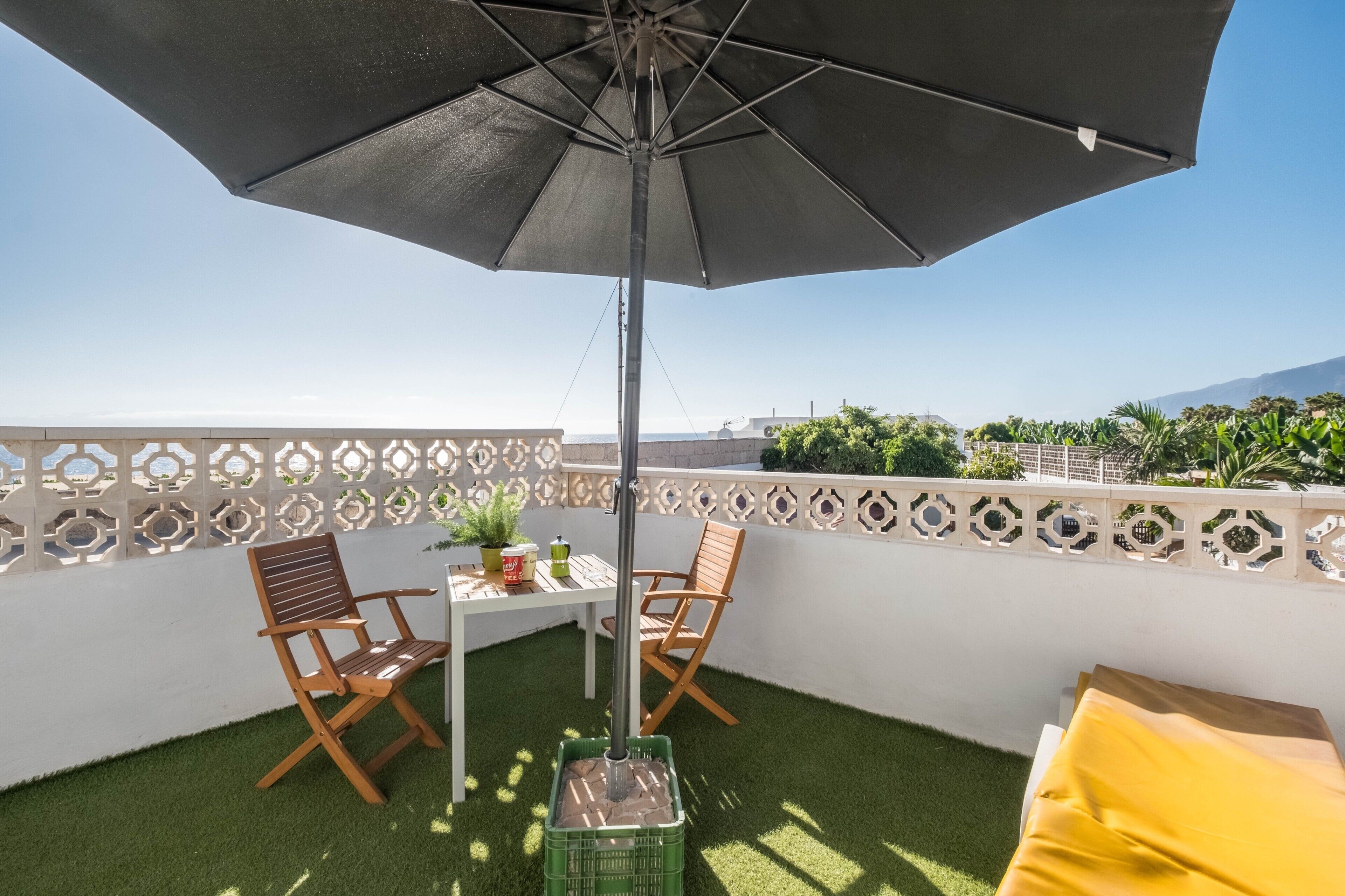 En balkon med et bord, to stole, en potteplante og en stor parasol.