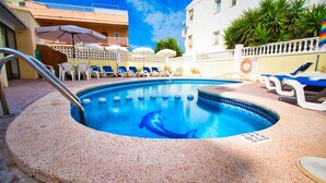 A swimming pool with lounge chairs and umbrellas, surrounded by a white fence and buildings. - Apartamentos Bon Aire - 13 (Peguera)