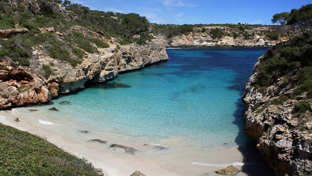 A coastal landscape with clear turquoise waters, rocky cliffs, and a sandy beach. - Apartamentos Bon Aire - 13 (Peguera)
