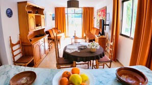 A dining area with a round table set for four, surrounded by wooden chairs. A buffet cabinet is to the left, and a television is mounted on the wall to the right. - Apartamentos Bon Aire - 13 (Peguera)