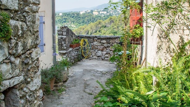 Un stretto sentiero in pietra che conduce a un edificio, con un muro in pietra da un lato e una facciata rossa dall'altro.