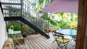 Un terrazzo in legno con tavolo e sedie, circondato da piante in vaso e una scala.