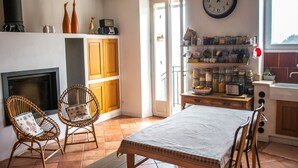 Un accogliente soggiorno con camino, poltrone in vimini, un tavolo da pranzo e un angolo cottura con barattoli e una sveglia.