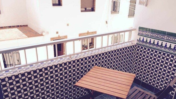 Ein Balkon mit einer Wand mit Muster, einem Holztisch und zwei Stühlen.