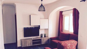 Ein Wohnzimmer mit Flachbildfernseher, einer Holzunterhaltungsecke, einem roten Sofa und einem Fenster mit Vorhängen.