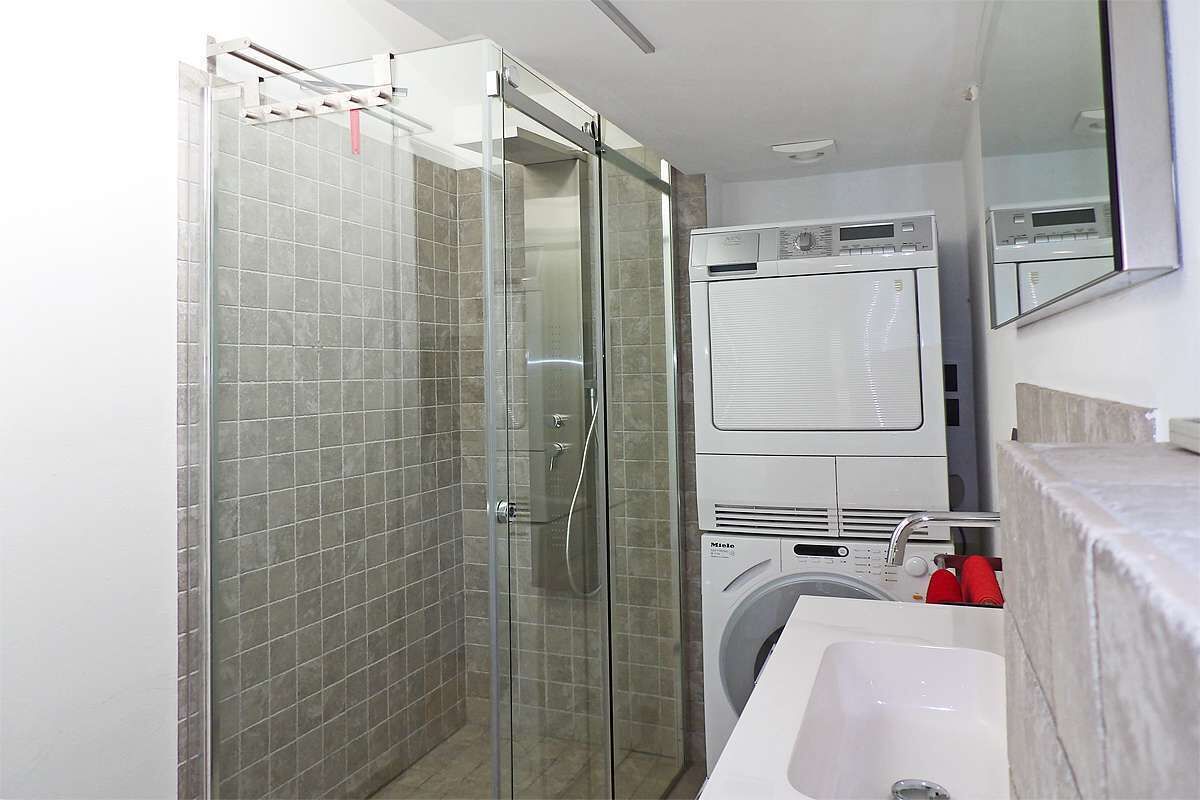 Un bagno compatto con doccia vetro, lavatrice e lavandino.