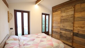 A bedroom with two beds, wooden paneling on one wall, and large windows.