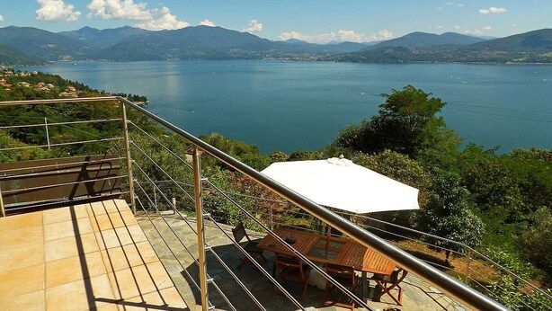 A terrace with a table and chairs, overlooking a lake with mountains in the background.