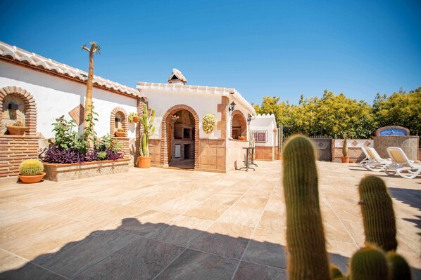 A courtyard with a building featuring arched doorways, a tiled floor, and potted plants.