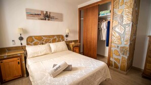 Quarto bem arrumado com cama, mesas de cabeceira, guarda-roupa e um detalhe decorativo na parede.