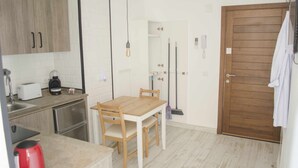 A compact kitchen with a wooden table and chairs, a coffee maker, a toaster, and a red kettle.